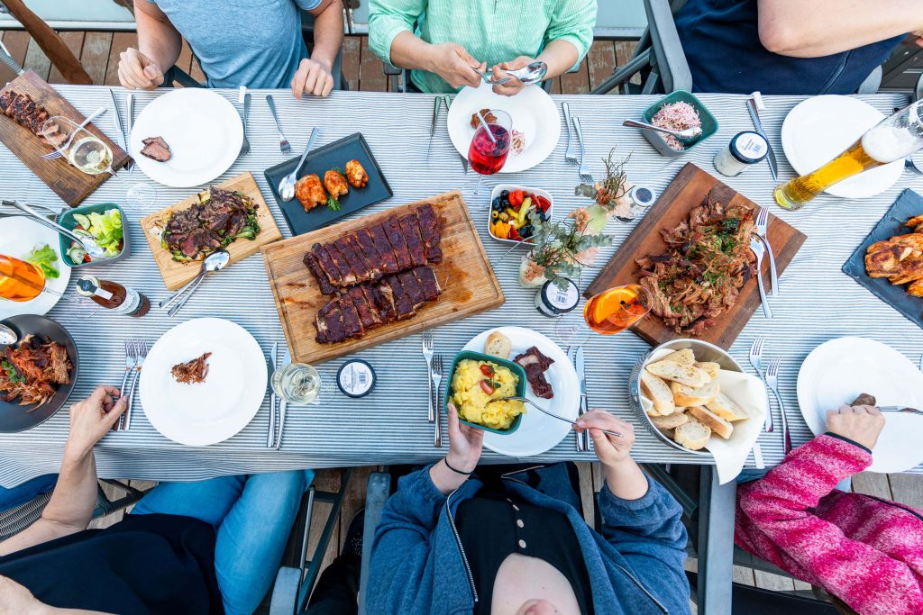 Gedeckter Tisch einer Grillparty. Darum sitzen Freunde und feiern.